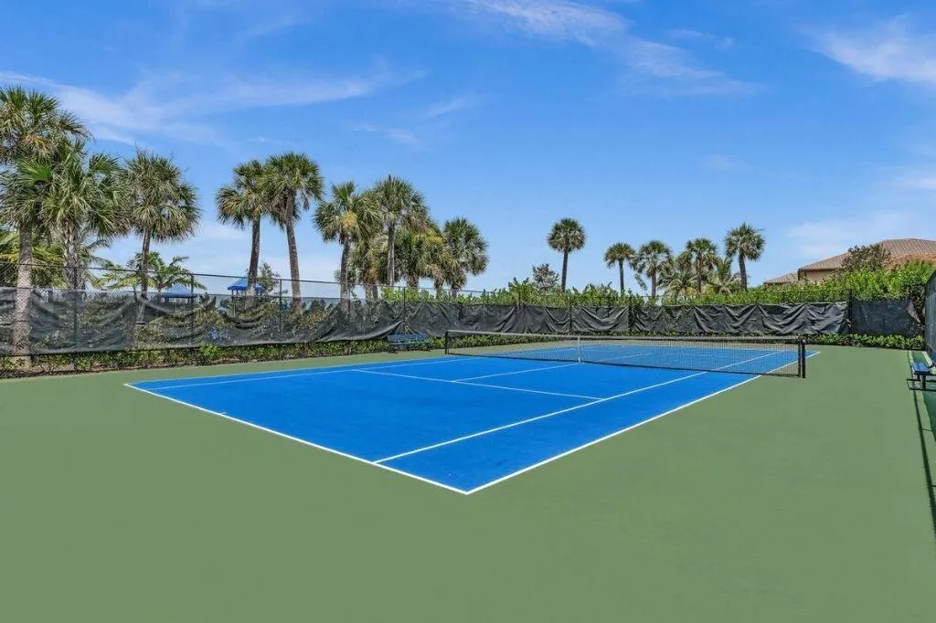 Full-size tennis court featuring a blue playing surface and green surrounding area