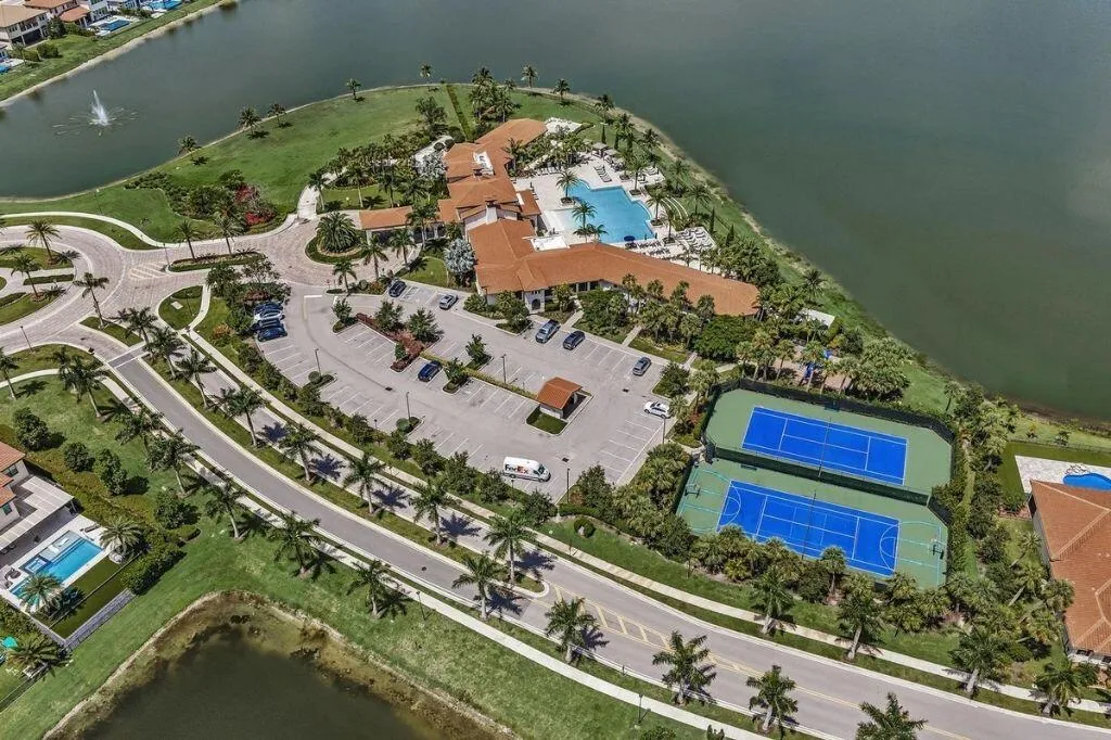 Extensive recreational facilities featuring two tennis courts, a large swimming pool, and a clubhouse with traditional tile roofing, all positioned alongside a substantial body of water
