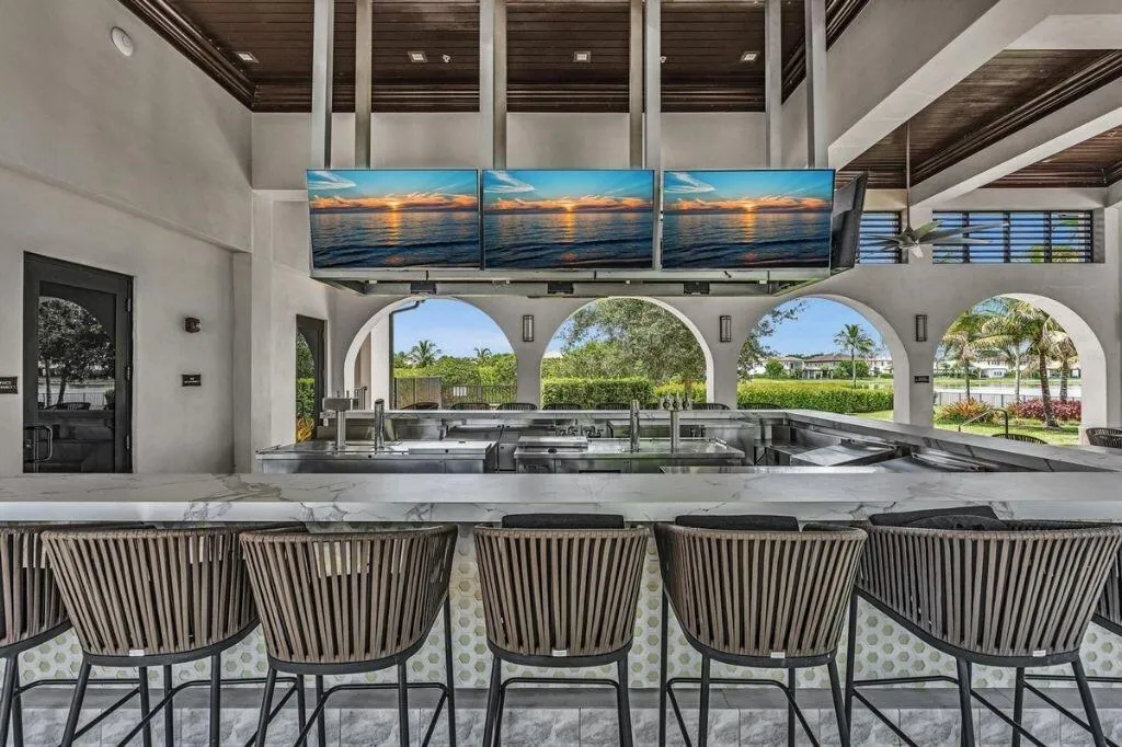 Outdoor bar area featuring a marble-look countertop, integrated stainless steel appliances, and multiple ceiling-mounted display screens