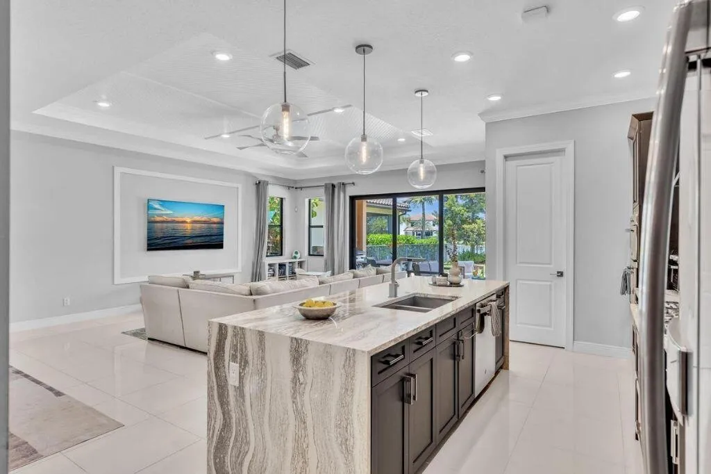 Open-concept kitchen featuring an expansive island with stone countertops, dark wood-finish cabinetry, and three pendant lights