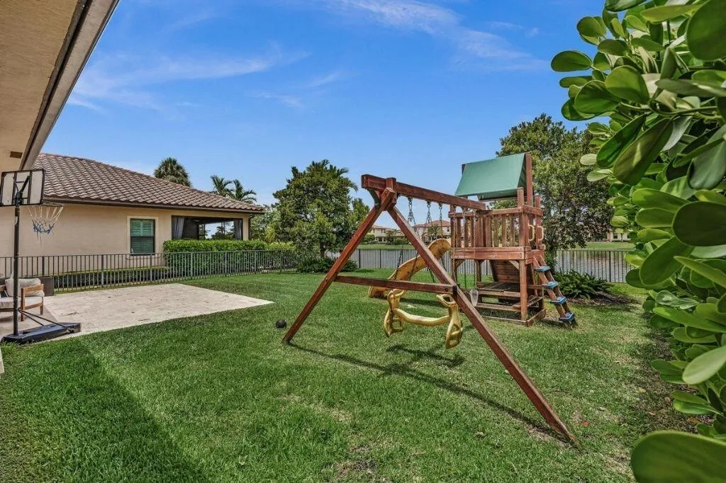 Expansive green lawn with a patio area, bordered by a privacy hedge and a metal fence