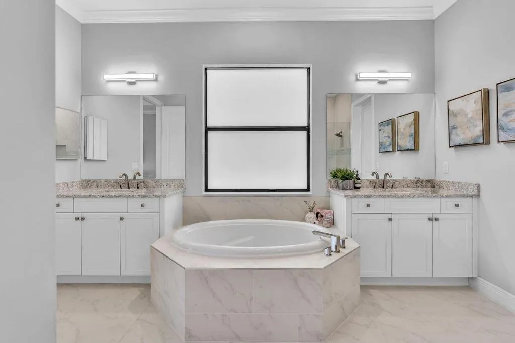 Soaking tub set in a tiled surround, flanked by two vanity cabinets with stone countertops and undermount sinks