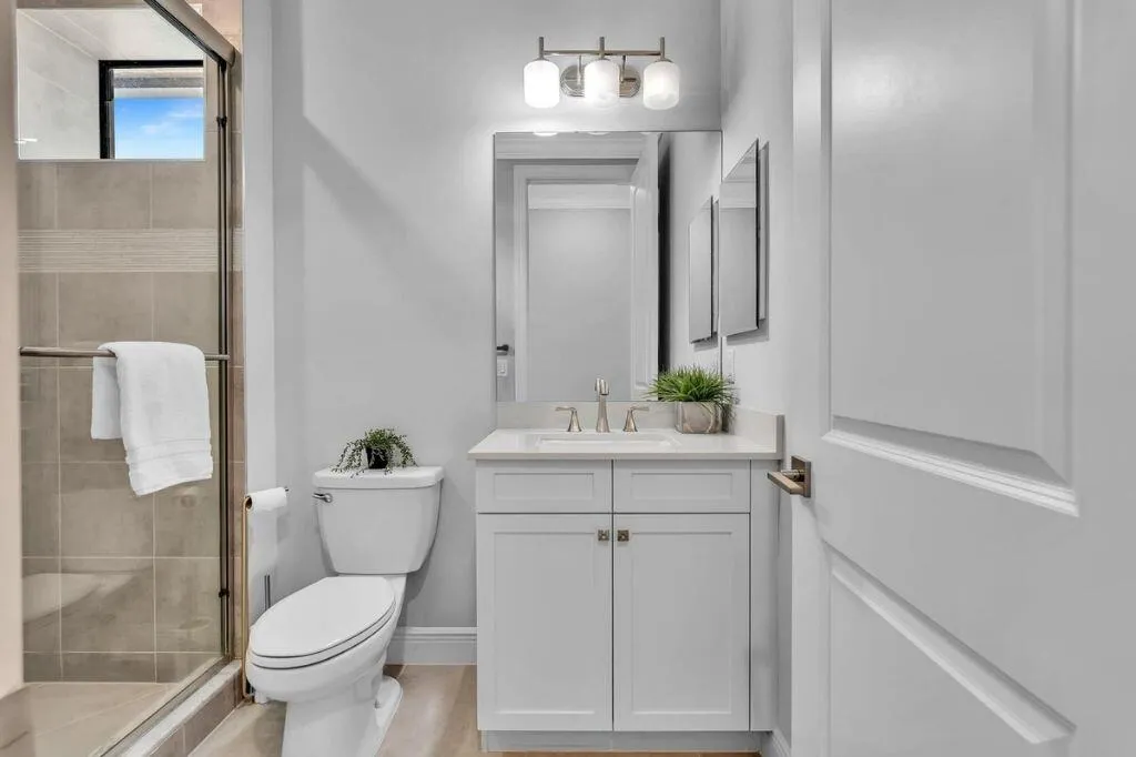 Bathroom featuring a glass-enclosed shower with tiled walls and a transom window, a white vanity with a countertop, a rectangular mirror, a three-light fixture, and wood-finish flooring