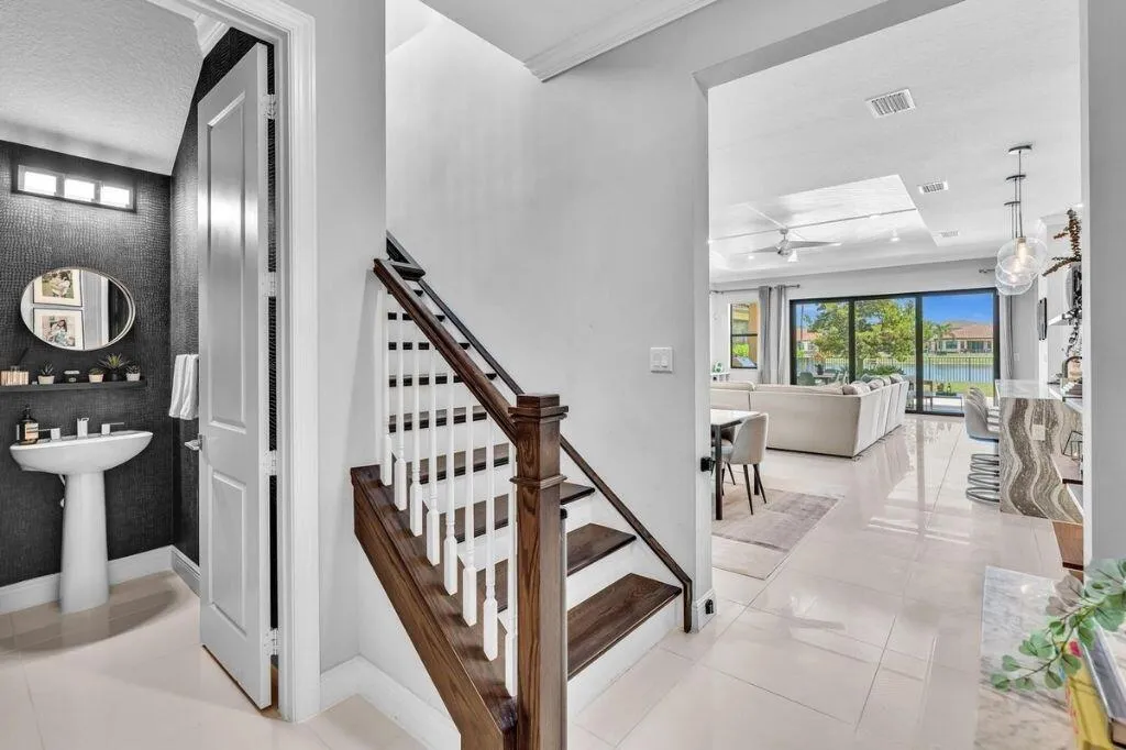 Hardwood staircase with white balusters, porcelain tile flooring, and a modern half-bath featuring a pedestal sink and dark textured wall covering