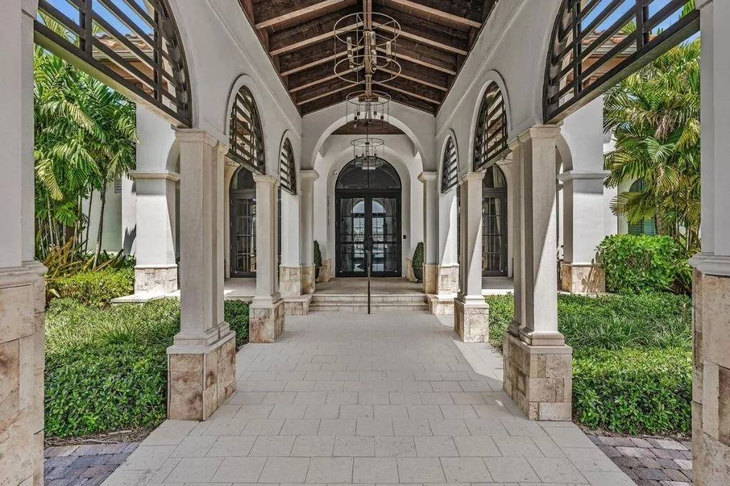 Arched portico entry with natural stone columns, wood ceiling beams, and a grand double-door entrance