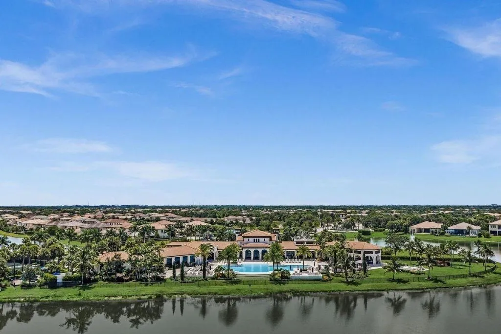 Lakeside property featuring a resort-style swimming pool with integrated spa, expansive paver decking, multiple covered lounge areas, and mature landscaping