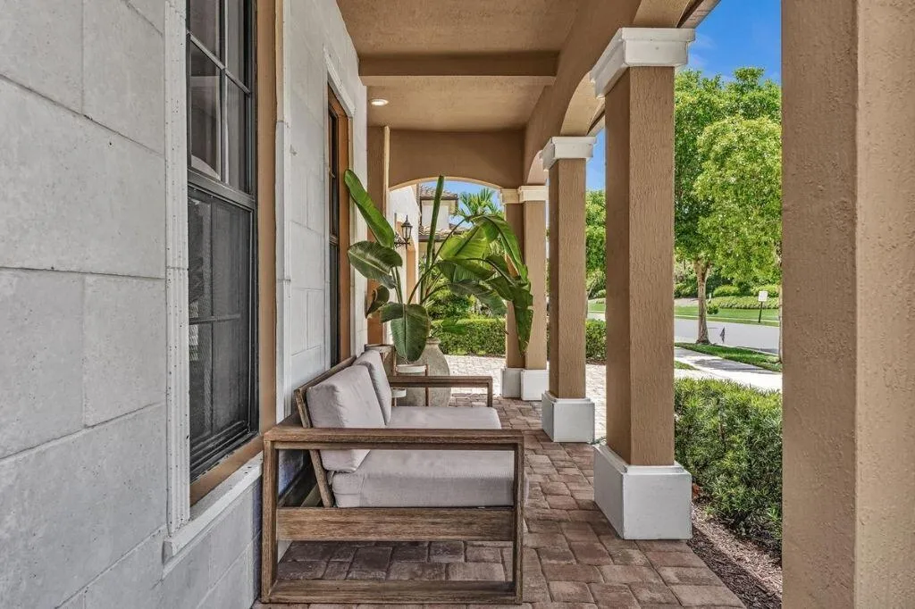 Covered front porch featuring a brick paver floor, stucco columns with white bases and caps, and a light-colored exterior wall with a dark-framed window
