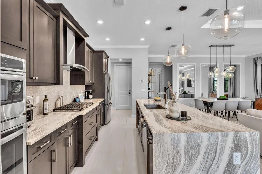 Gourmet kitchen featuring a waterfall island with integrated sink, stainless steel appliances, dark wood cabinetry, and recessed lighting