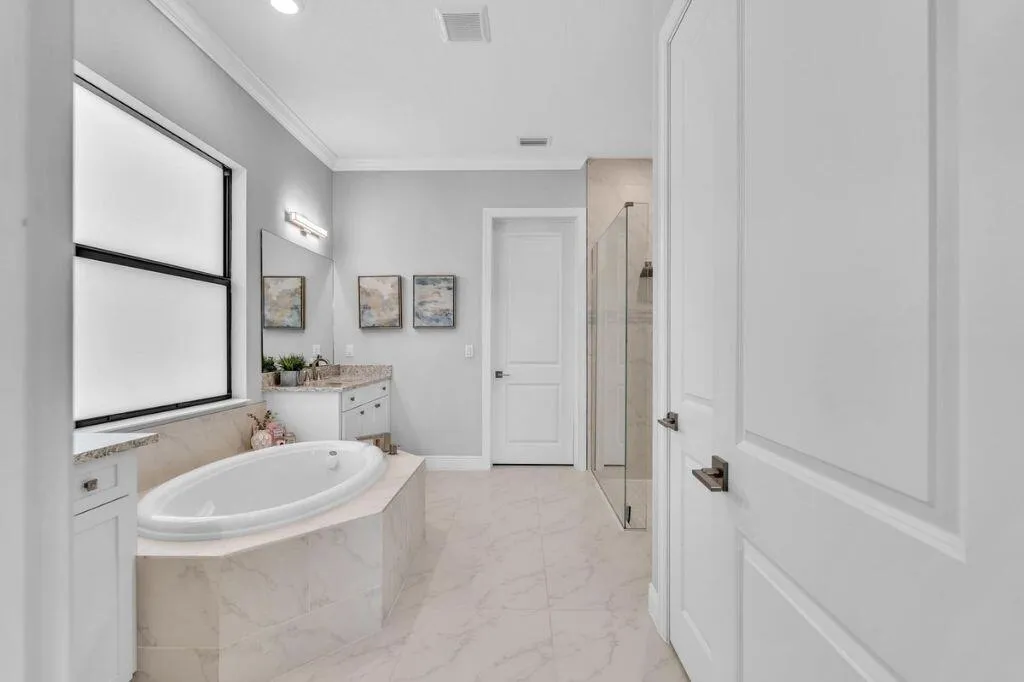 Soaking tub with tiled surround, large window, and light-toned flooring