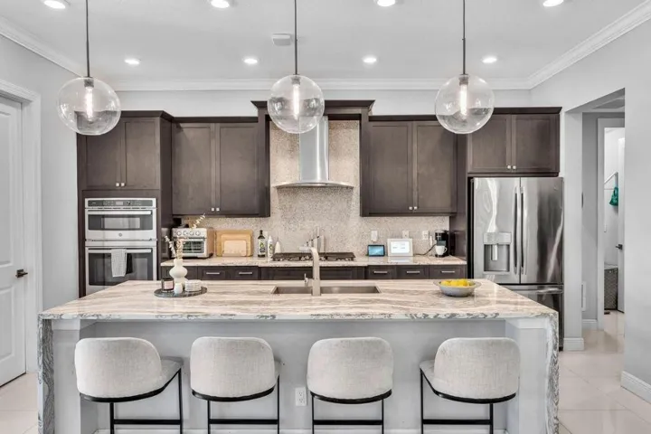 Kitchen featuring a large island with seating, stainless steel appliances, dark wood-finish cabinetry, a tile backsplash, and recessed lighting