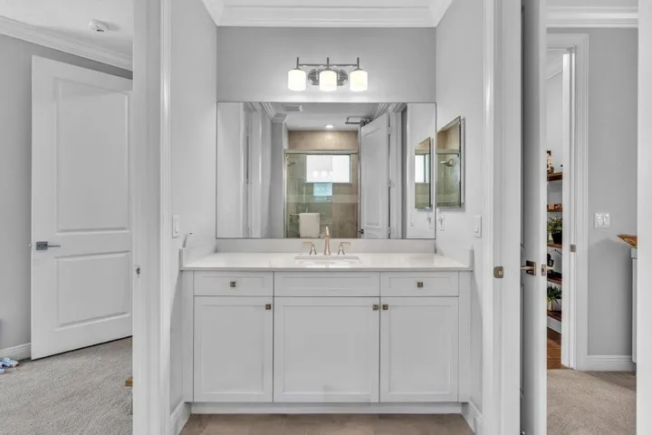Bathroom vanity featuring white cabinetry, a light-toned countertop, and an integrated rectangular sink with a gold-tone faucet
