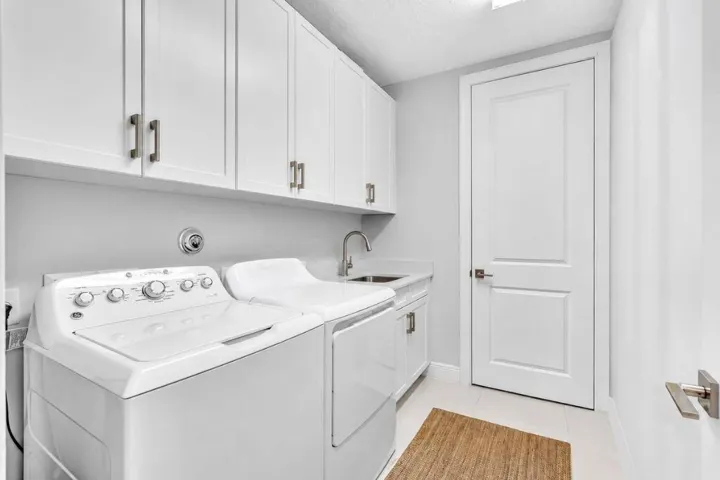 Dedicated laundry room featuring white cabinetry with brushed nickel hardware, a utility sink with a brushed nickel faucet, and light tile flooring