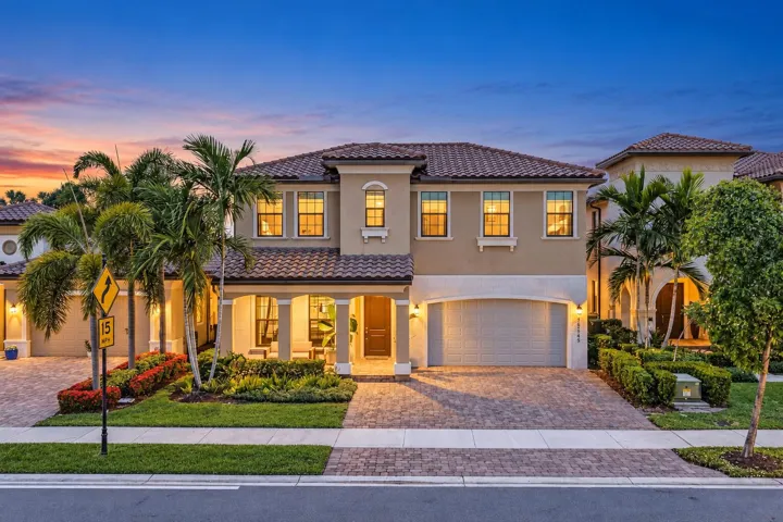 Mediterranean-style residence featuring a tile roof, stucco exterior, two-car garage, paver driveway, and mature palm trees