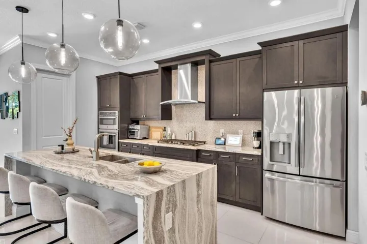 Gourmet kitchen featuring a waterfall island with stone countertop, stainless steel appliances, dark wood cabinetry, and recessed lighting