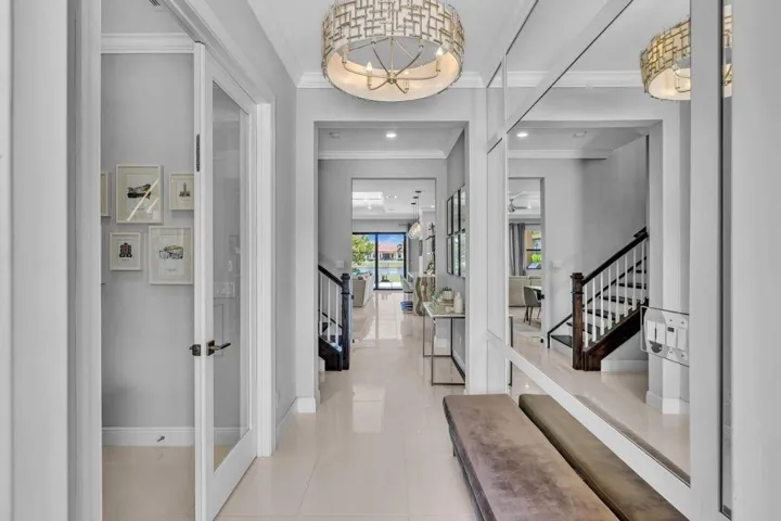 Grand entryway featuring a decorative ceiling fixture, tiled flooring, glass-paneled interior doors, and a dark wood-finish staircase with white risers
