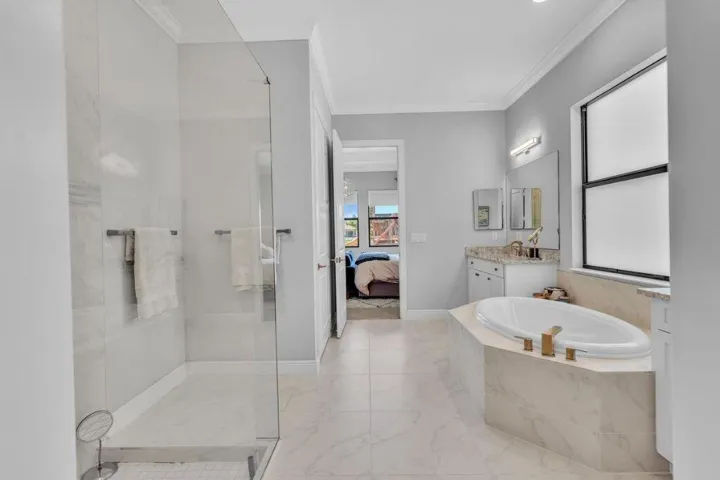 Spacious bathroom featuring a frameless glass shower enclosure, a built-in soaking tub with gold-tone fixtures, a vanity with a stone countertop, and tile flooring