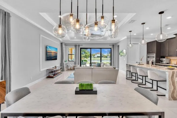 Spacious open-concept interior featuring light tile flooring, an ornate tray ceiling with contemporary pendant lighting, and a kitchen island with stone detailing