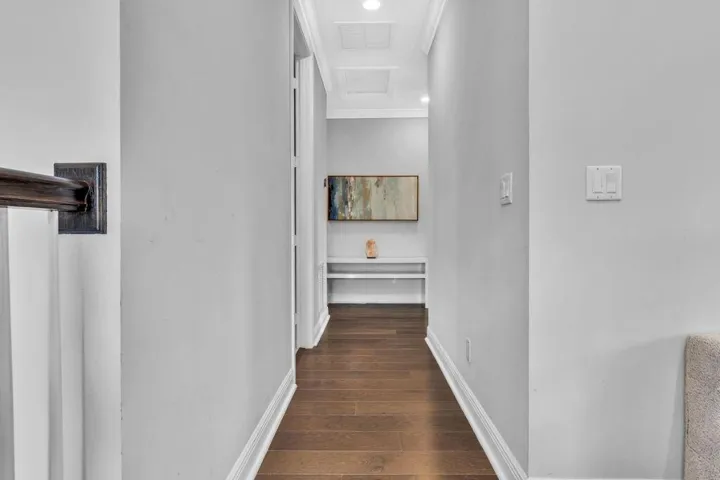 Hallway featuring wood-finish flooring, light gray wall paint, white baseboards, and crown molding