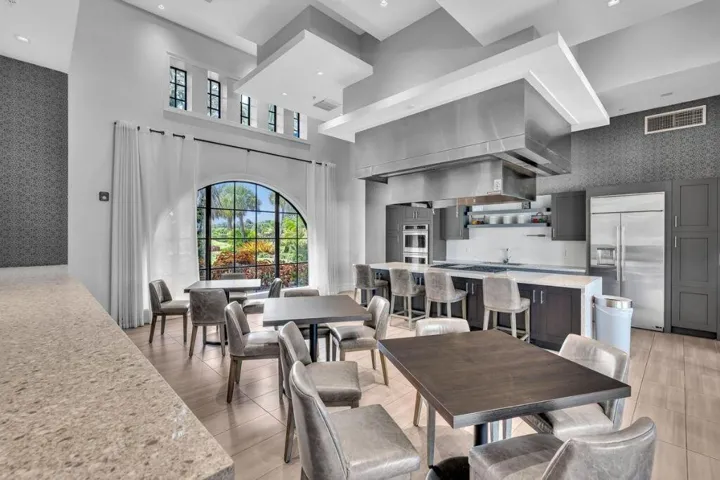 Spacious kitchen and dining area featuring a large arched window, vaulted ceilings, a substantial kitchen island with seating, a commercial-grade range hood, and integrated stainless steel appliances
