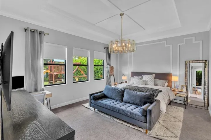 Spacious room featuring a tray ceiling with crown molding, a decorative chandelier, and three large windows