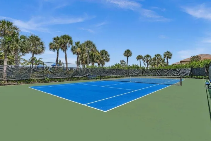 Full-size tennis court featuring a blue playing surface and green surrounding area
