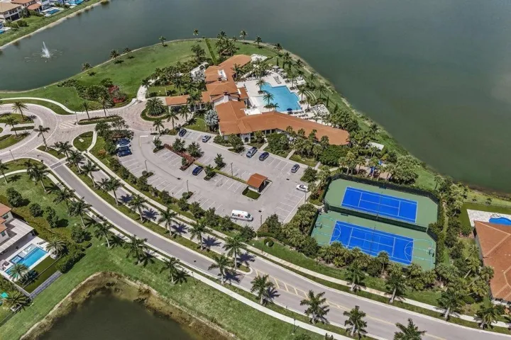 Extensive recreational facilities featuring two tennis courts, a large swimming pool, and a clubhouse with traditional tile roofing, all positioned alongside a substantial body of water