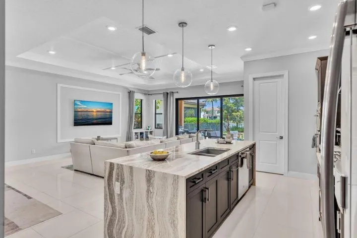 Open-concept kitchen featuring an expansive island with stone countertops, dark wood-finish cabinetry, and three pendant lights