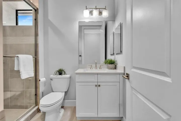 Bathroom featuring a glass-enclosed shower with tiled walls and a transom window, a white vanity with a countertop, a rectangular mirror, a three-light fixture, and wood-finish flooring