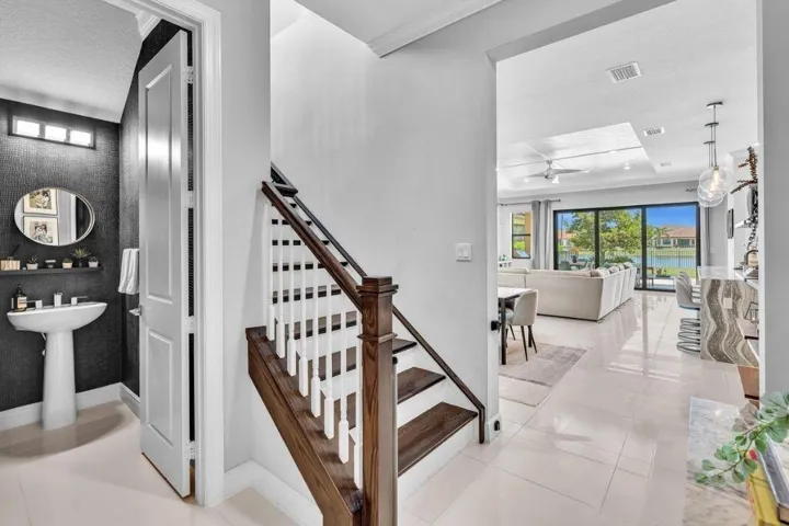 Hardwood staircase with white balusters, porcelain tile flooring, and a modern half-bath featuring a pedestal sink and dark textured wall covering