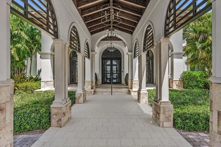 Arched portico entry with natural stone columns, wood ceiling beams, and a grand double-door entrance