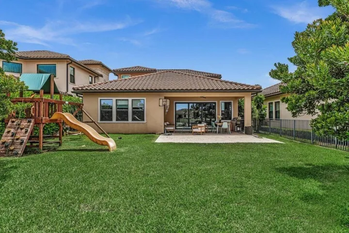 Expansive grassy yard featuring a covered patio, tiled roof, and stucco exterior