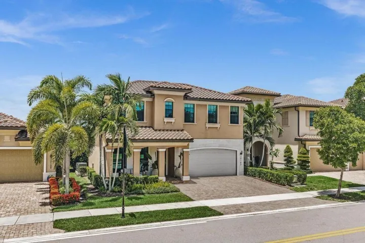 Mediterranean-style residence featuring a tile roof, stucco exterior, multiple arched windows, mature palm trees, and a paver driveway
