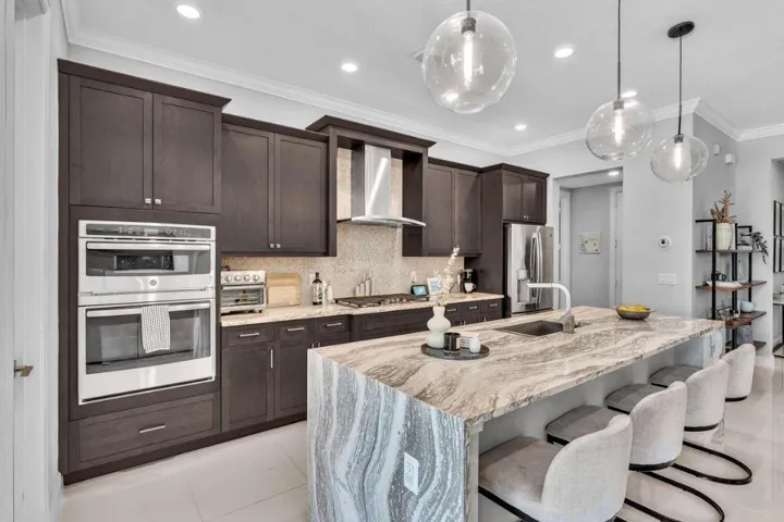 Gourmet kitchen featuring a waterfall island with integrated seating, dark wood cabinetry, stainless steel appliances, and pendant lighting