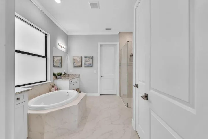 Soaking tub with tiled surround, large window, and light-toned flooring