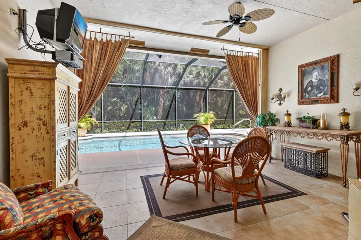 Tiled flooring throughout this space features a ceiling fan, a screened enclosure, and an in-ground pool