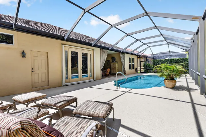 Screened enclosure with a free-form swimming pool, concrete patio, and exterior access via double French doors
