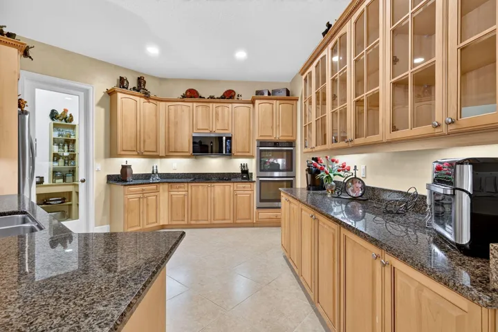 Kitchen featuring extensive wood cabinetry, granite countertops, tile flooring, and integrated stainless steel appliances