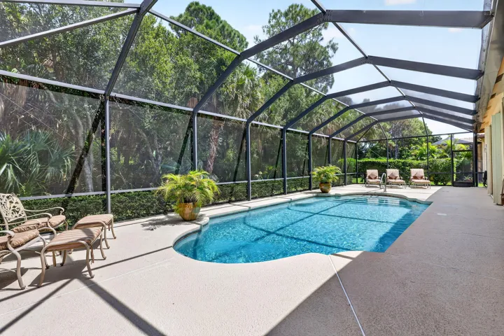Screened-in outdoor living space featuring a blue-tiled swimming pool and a light-colored deck