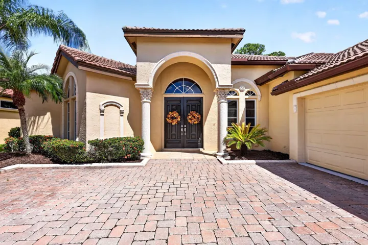 Stucco exterior with a tile roof, arched entryway, decorative columns, and a paver driveway