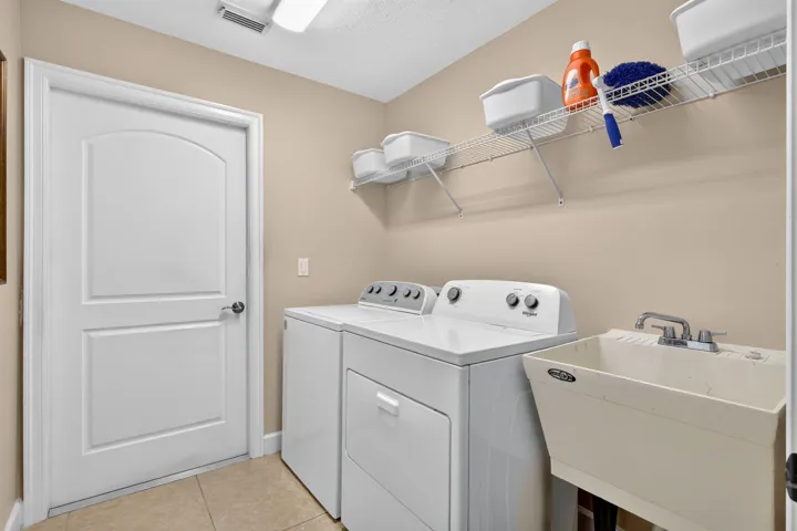 Dedicated laundry area featuring a utility sink, overhead wire shelving, and tile flooring