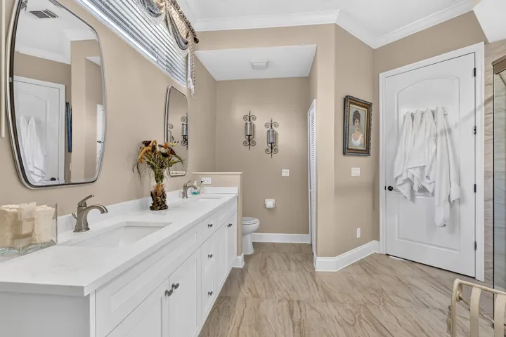 Dual vanity with white cabinetry, brushed nickel faucets, and stone-look flooring