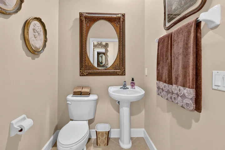 Pedestal sink with chrome-finish faucet, traditional oval mirror with an ornate frame, and tile flooring