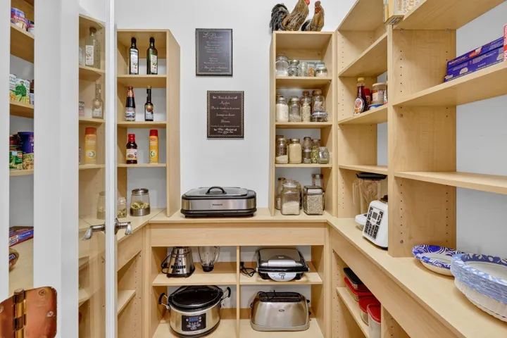 Walk-in pantry featuring light wood-finish shelving, built-in countertop space, and white walls