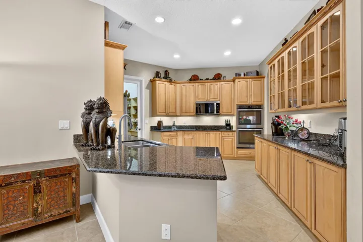 Kitchen featuring a peninsula with integrated sink, wood cabinetry, granite countertops, tile flooring, and stainless steel double ovens