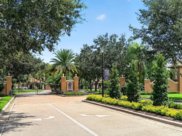 Gated community entrance with decorative columns, wrought iron gates, and mature landscaping