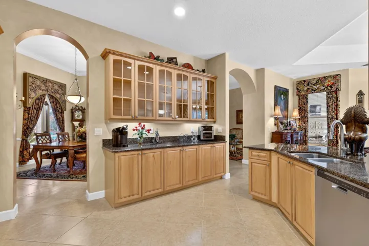 Arched entryway, built-in cabinetry with glass fronts, granite-style countertops, integrated dishwasher, and tile flooring