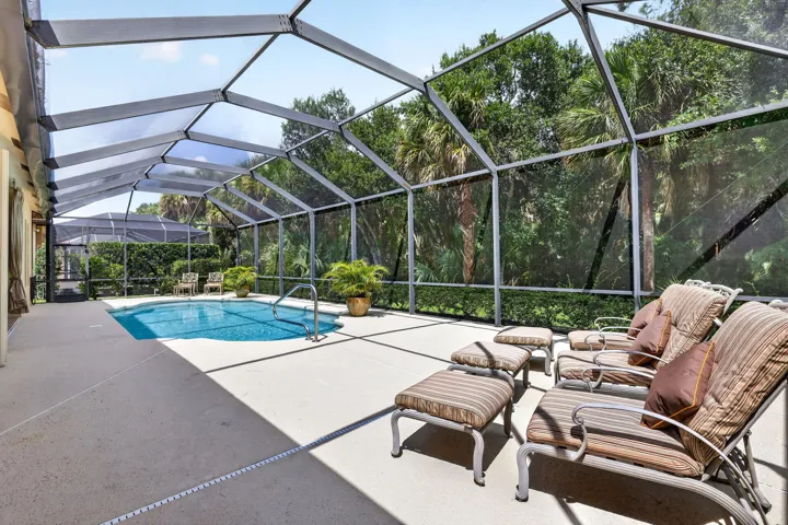 Screened enclosure with an in-ground swimming pool, concrete patio, and lush mature trees