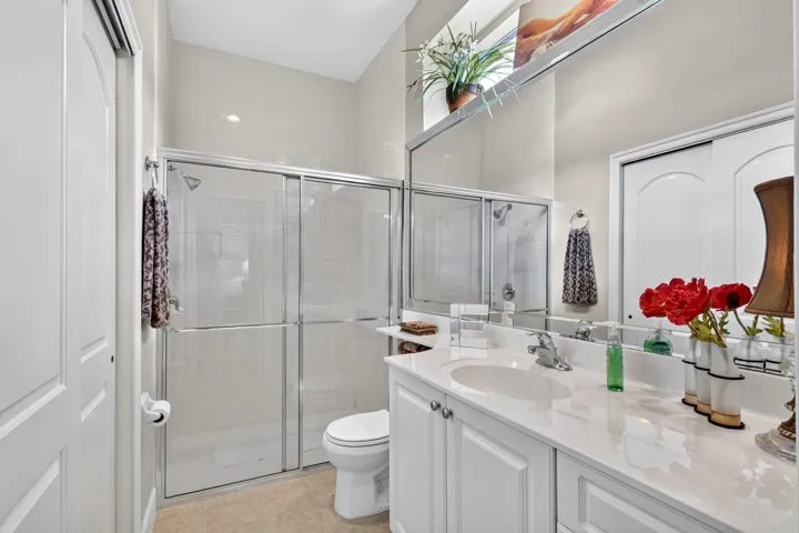 White vanity with a single basin sink and a light-toned countertop, framed mirror, glass-enclosed shower