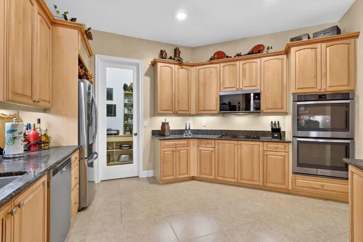 Kitchen featuring light wood cabinetry, dark stone countertops, stainless steel appliances, and a walk-in pantry with a glass-paneled door