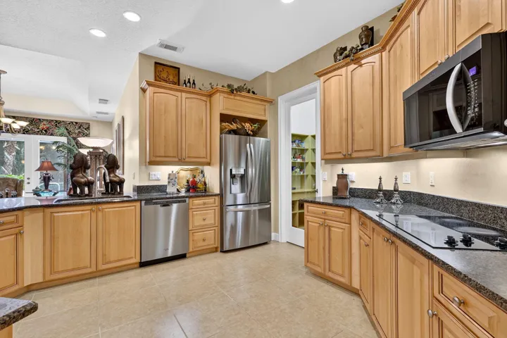 Kitchen with wood cabinetry, stainless steel appliances, dark stone countertops, tile flooring, and recessed lighting